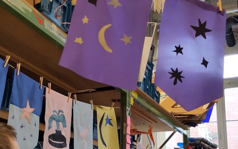A row of colourful flags signals the installation from far and welcomes future visitors: they were designed and made by the young makers, but also wider community members, invited to contribute during a family workshop.