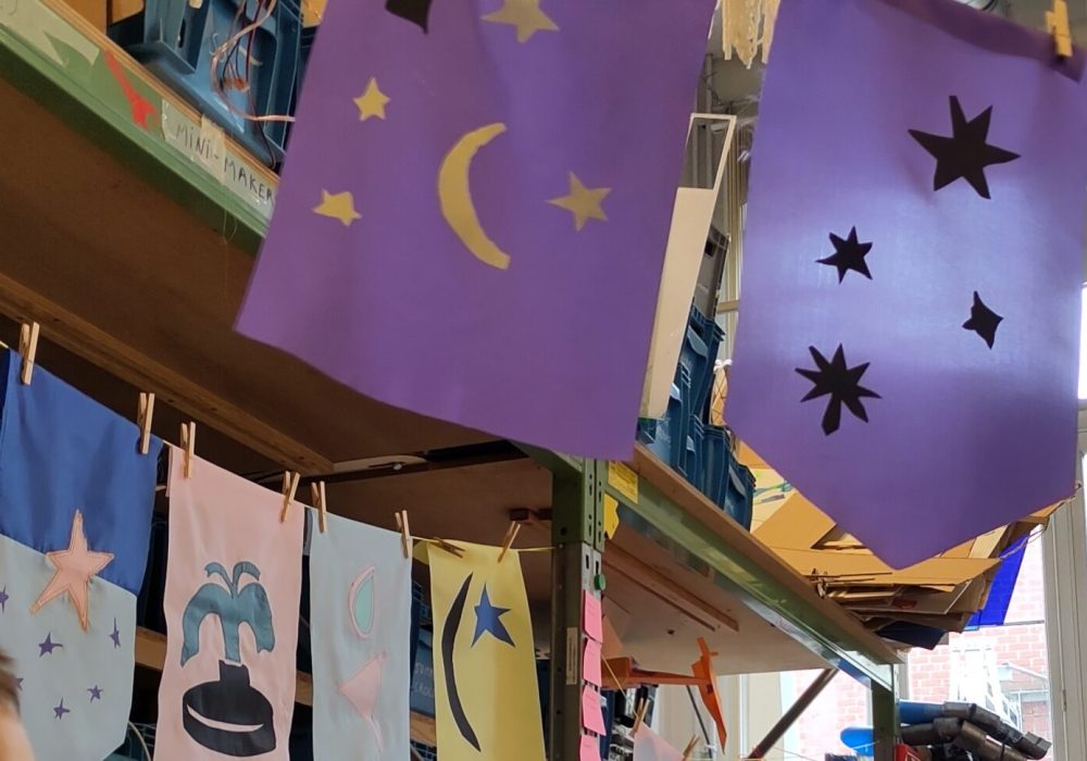 A row of colourful flags signals the installation from far and welcomes future visitors: they were designed and made by the young makers, but also wider community members, invited to contribute during a family workshop.